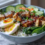 Golden tofu and soft jammy eggs sit atop steamed rice with crisp veggies in a Tofu Jammy Egg Breakfast Bowl.  