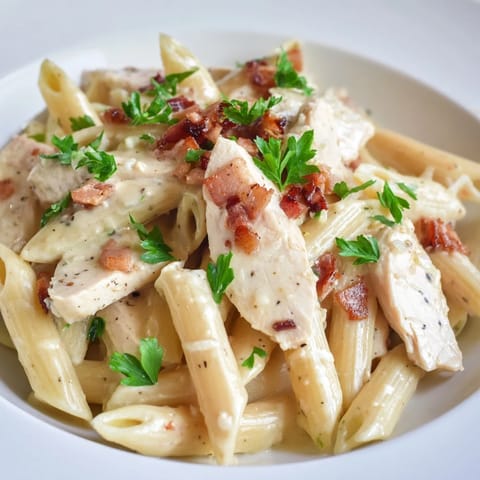Steam rises from a bowl of Creamy Chicken Bacon Penne featuring tender chicken and smoky bacon.