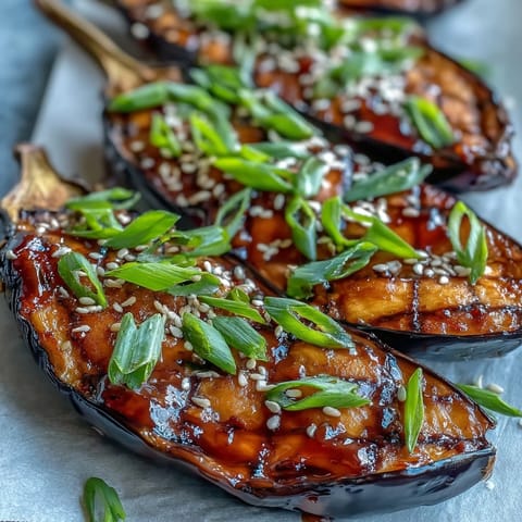 Golden-brown miso-glazed eggplant with a tender, velvety flesh and fresh green onion garnish on a rustic wooden table.  