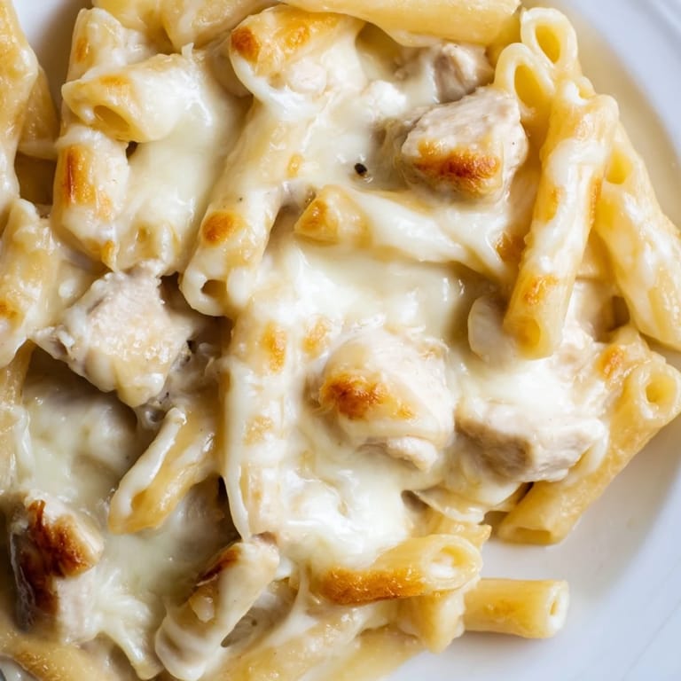 Close-up of Chicken Alfredo Casserole showing gooey cheese pull and creamy texture, paired with a crisp green salad on the side.