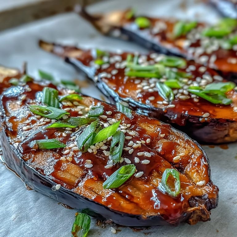 Caramelized miso-glazed eggplant halves topped with sesame seeds and sliced scallions, ready to be served with steamed rice.
