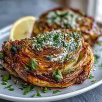 Golden roasted cabbage steaks, caramelized edges with a creamy tahini drizzle and fresh parsley garnish.
