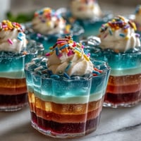 Vibrant rainbow Jello cups with colorful layers and whipped cream topping, perfect for kids' parties.  